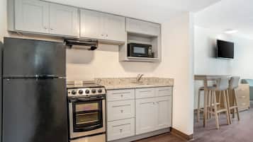 A kitchen with a refrigerator, oven, microwave, and a TV mounted on the wall.