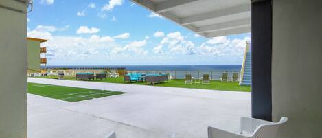 A covered outdoor area with a view of the ocean, a grassy lawn, and several seating areas.