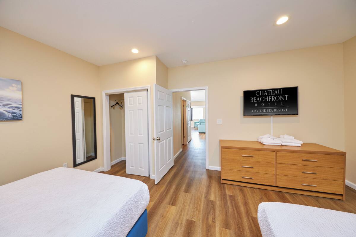 A hotel room with two beds, a wooden dresser, a mirror, and a sign indicating it's a beach resort.