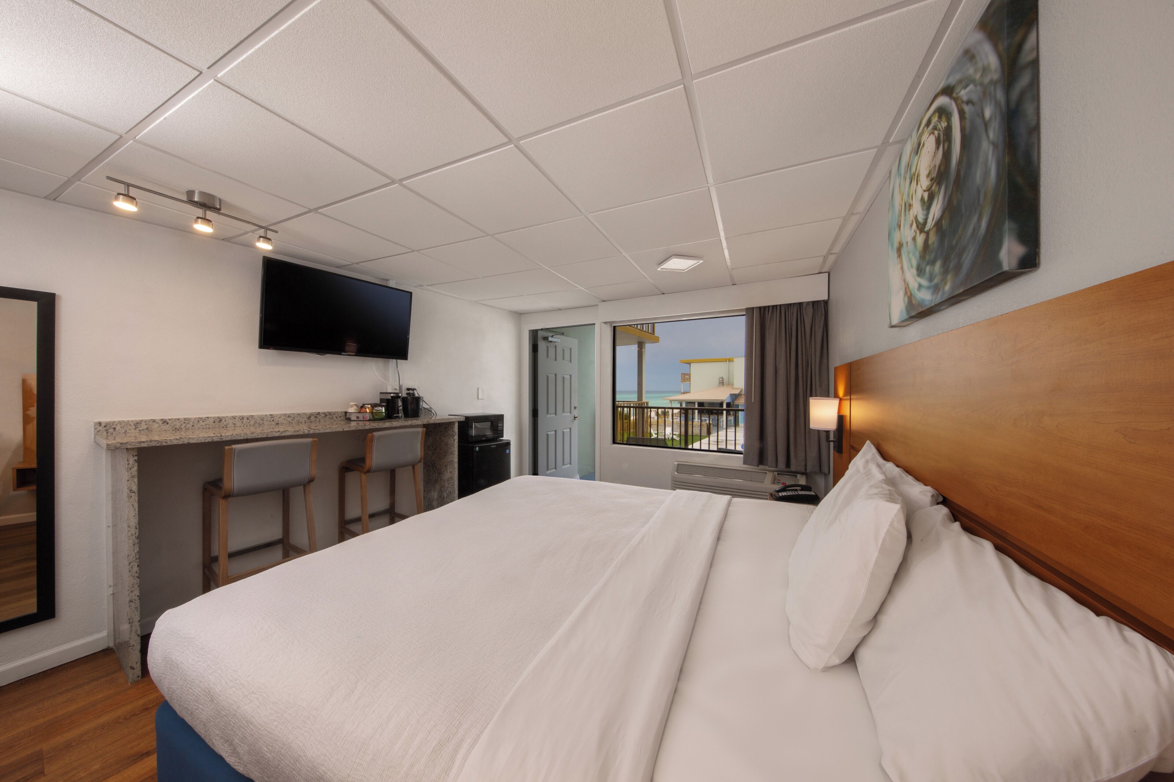 A hotel room with a bed, a desk with a chair, a TV mounted on the wall, and a window with a view.