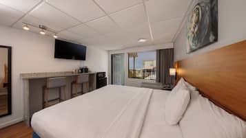Habitación de hotel con cama, escritorio con silla, televisor montado en la pared y ventana con vistas.