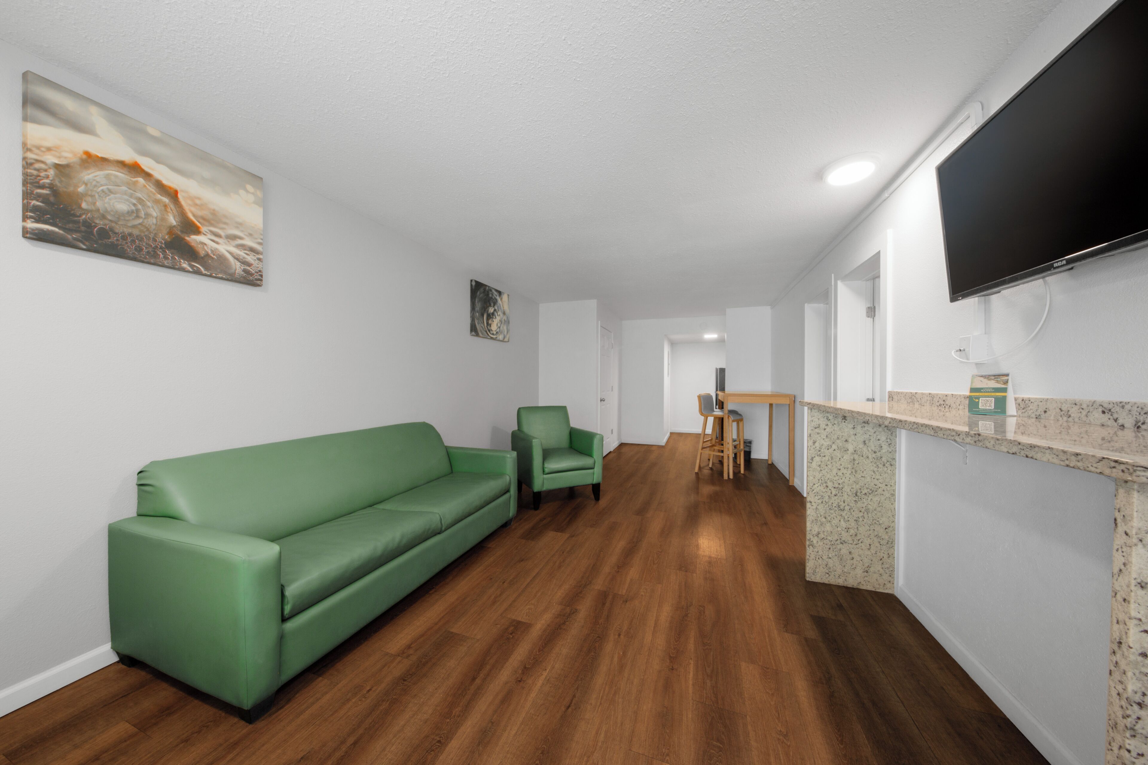 Una sala de estar moderna con un sofá verde, un sillón verde pequeño, una mesa de comedor de madera con sillas y un televisor de pantalla plana montado en la pared.