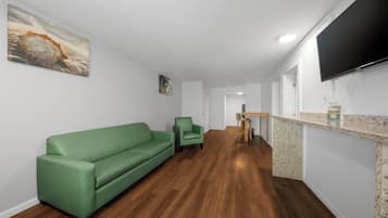 Una sala de estar moderna con un sofá verde, un sillón verde pequeño, una mesa de comedor de madera con sillas y un televisor de pantalla plana montado en la pared.