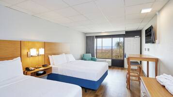 A hotel room with two beds, a desk, a chair, and a view of the outdoors.