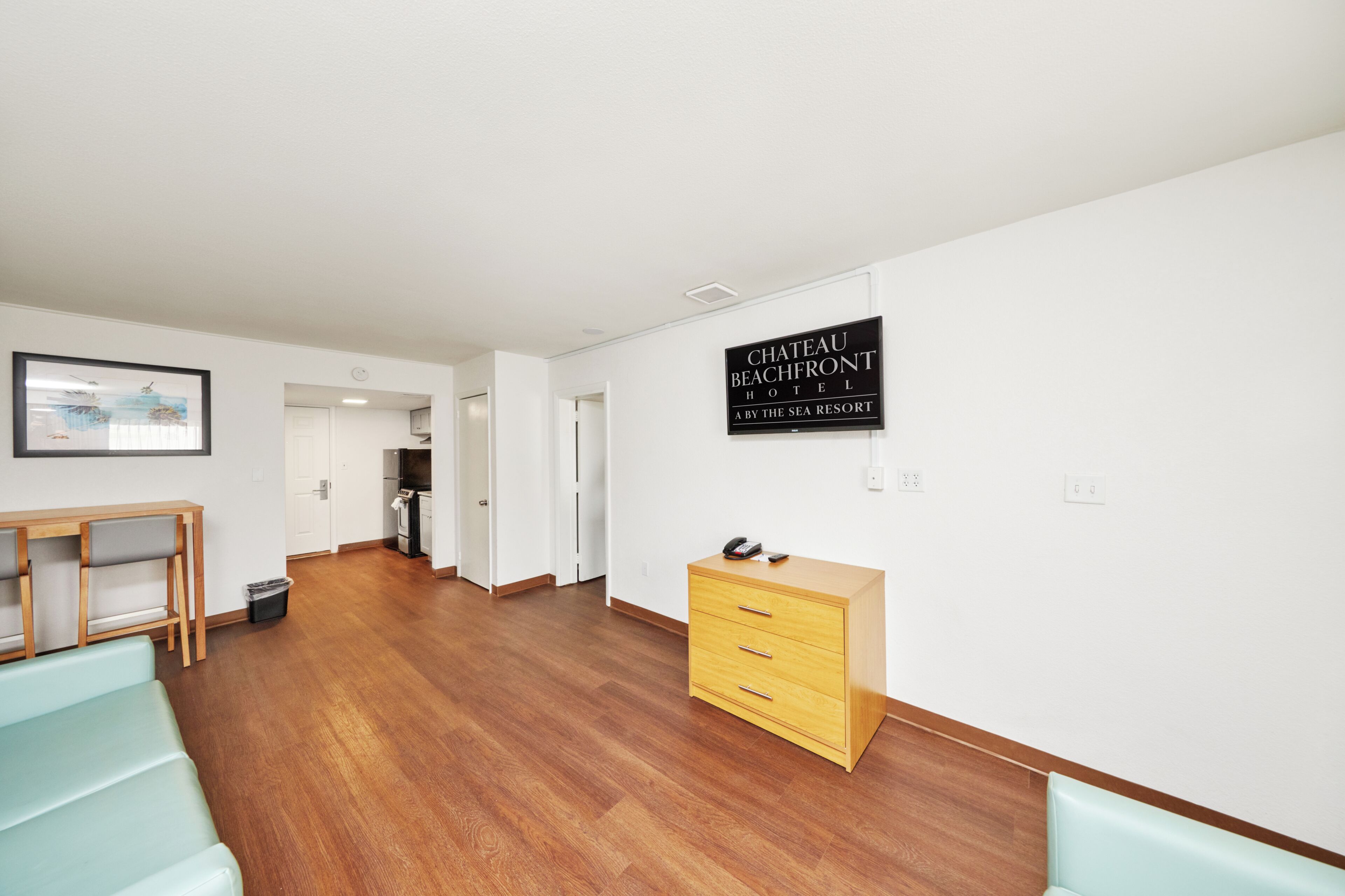 A hotel room with a wooden floor, a desk, a dresser, and a sign reading 'CHATEAU BEACHFRONT HOTEL.'