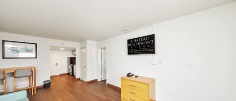 A hotel room with a wooden floor, a desk, a dresser, and a sign reading 'CHATEAU BEACHFRONT HOTEL.'