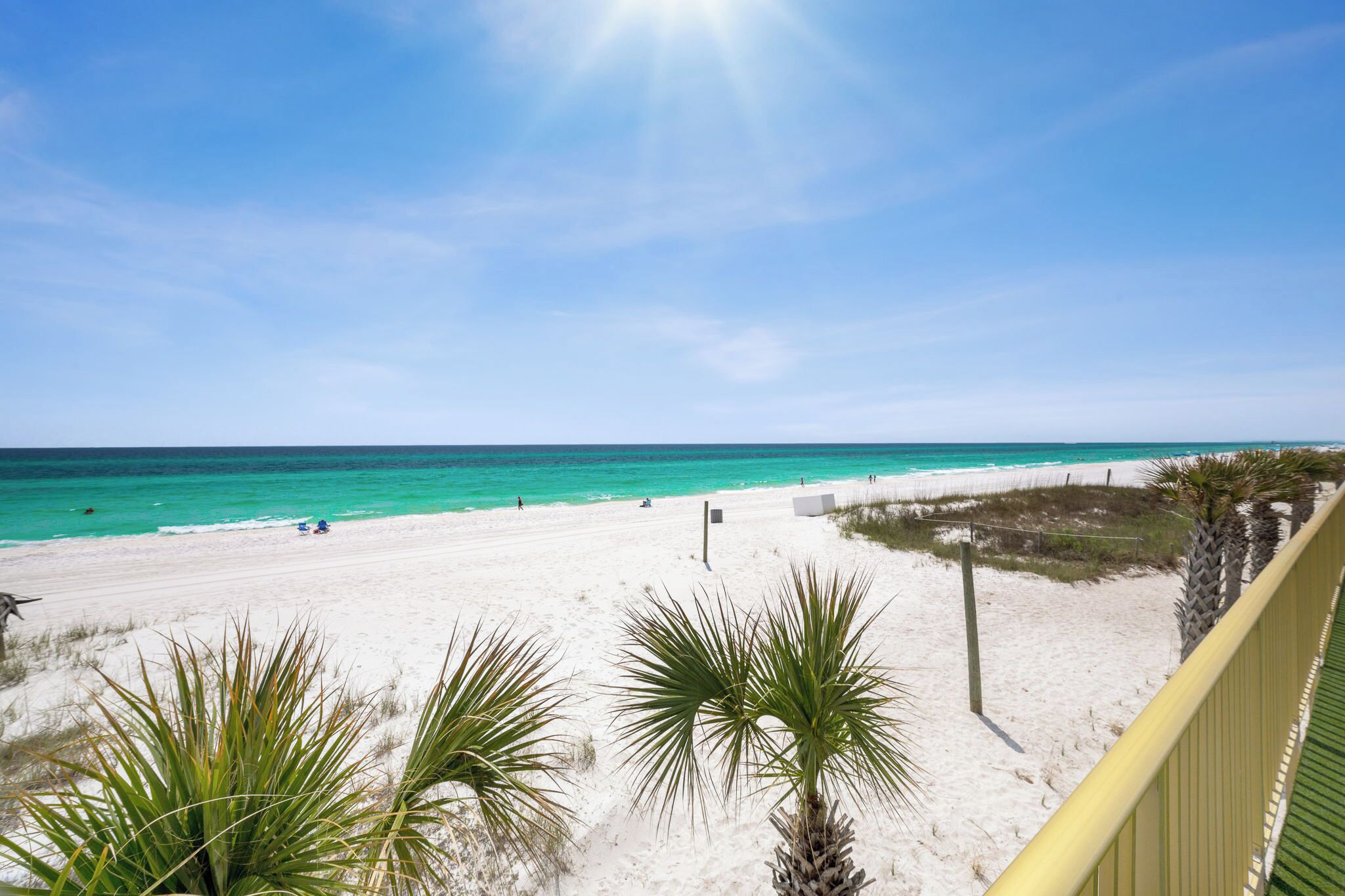 A beach with white sand, clear turquoise water, and a sunny sky.