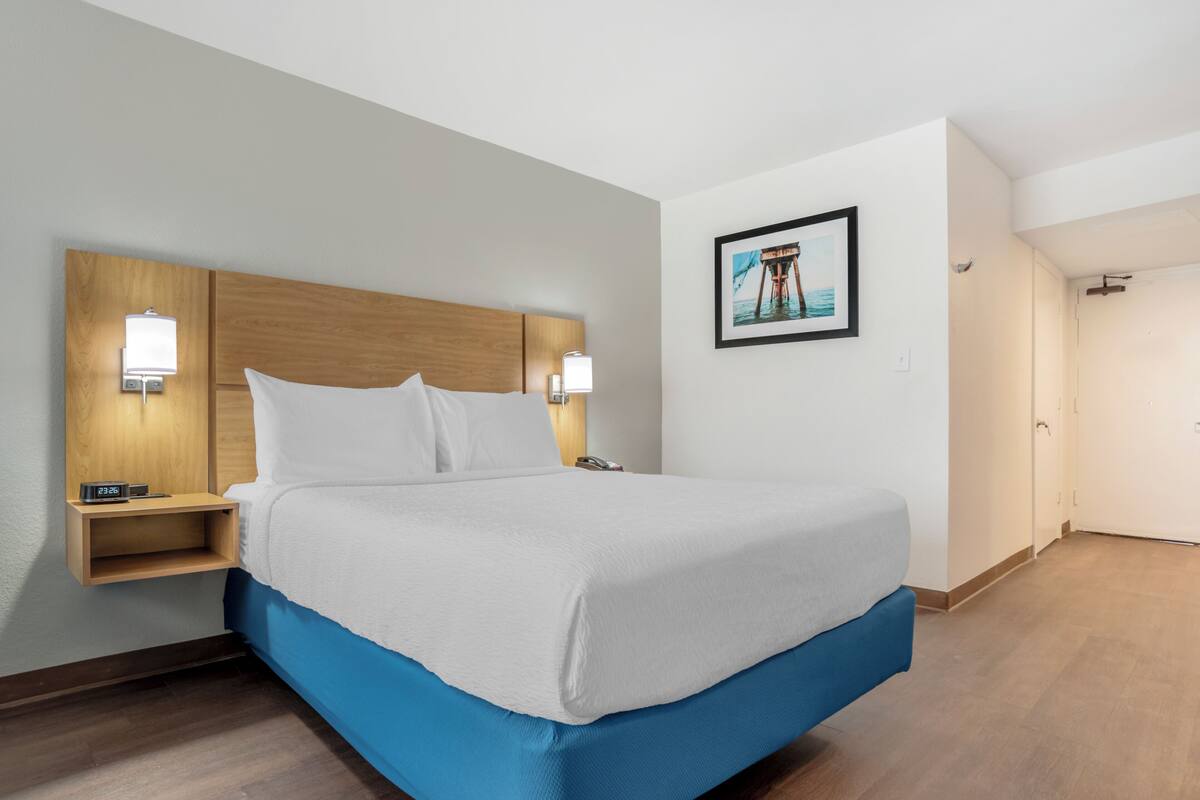 A hotel room with a bed, bedside lamps, a nightstand, a framed picture on the wall, and a door.