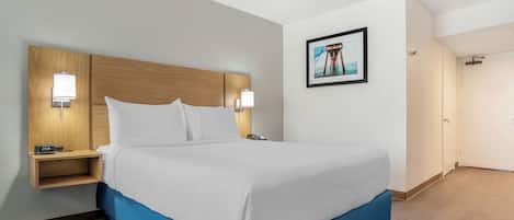 Habitación de hotel con cama, lámparas de noche, mesita de noche, un cuadro en la pared y una puerta.