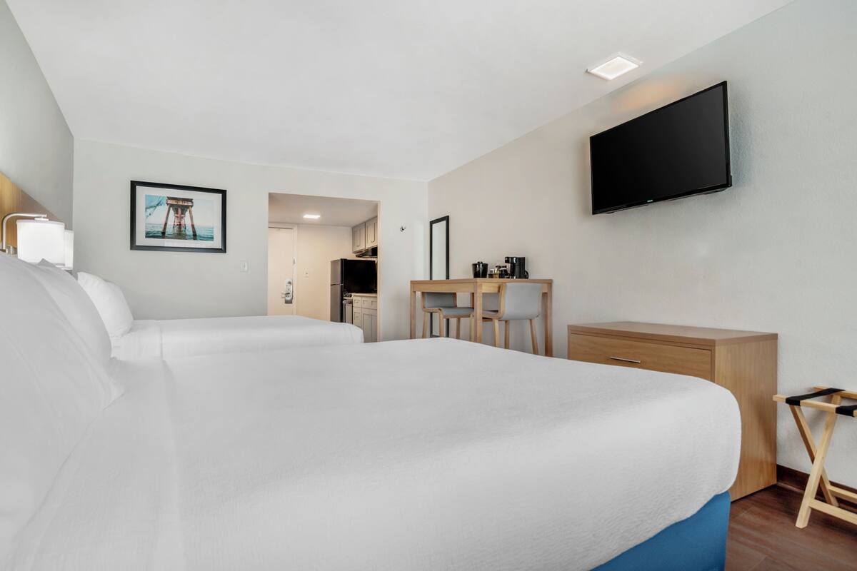 A hotel room with a large bed, a desk, a chair, a television, and a picture on the wall.