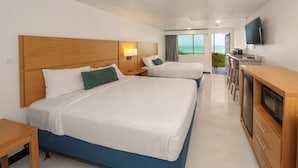 A hotel room with two beds, a TV, a kitchenette, and a view of the ocean.