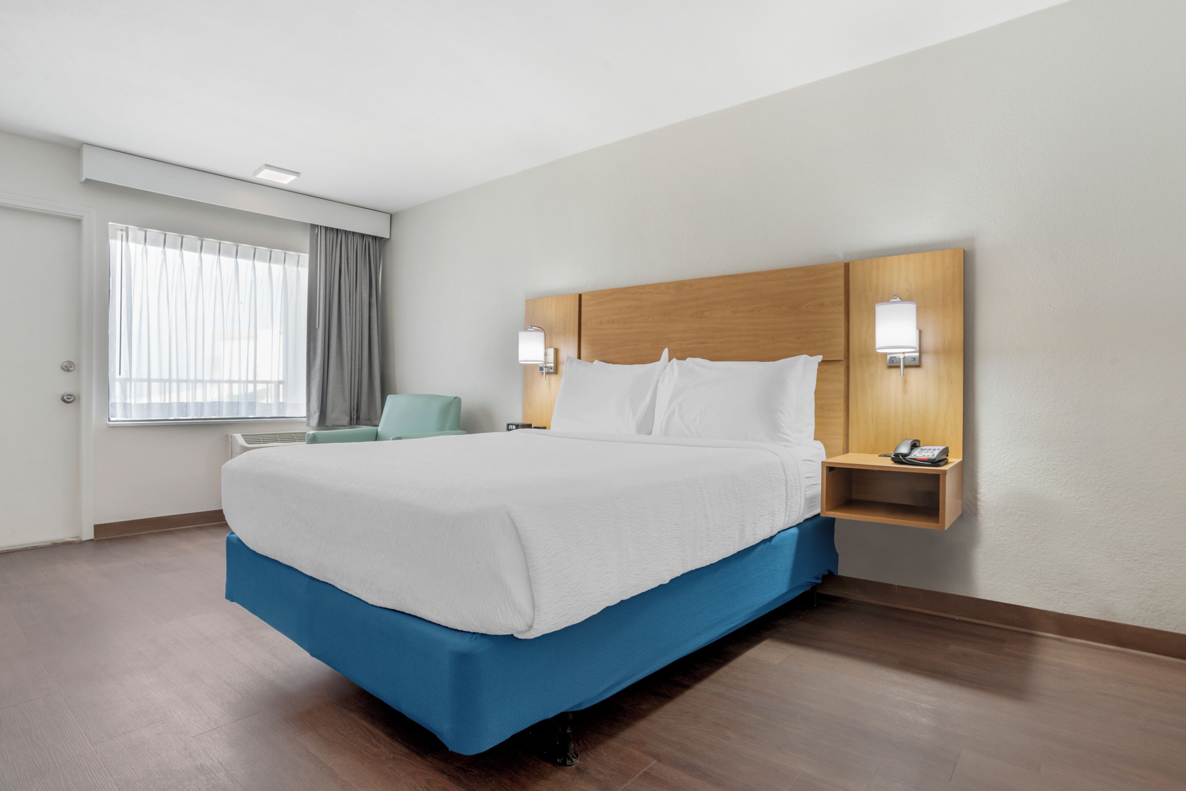 Ein Hotelzimmer mit Bett, Sessel, Nachttisch und einem fenster mit Vorhängen.