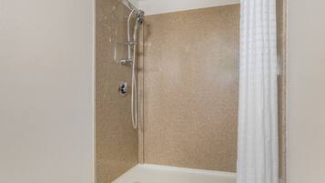 A shower with a handheld showerhead, a wall-mounted faucet, and a white shower curtain.