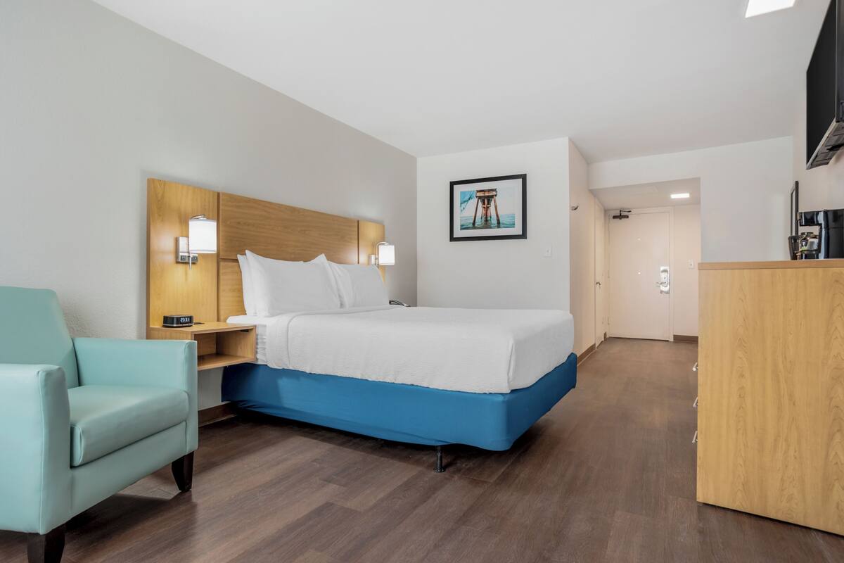 A hotel room with a bed, a nightstand, a lamp, a chair, and a desk.