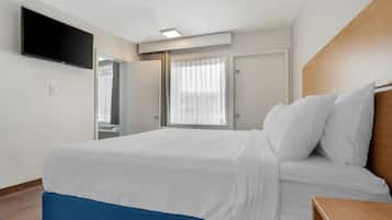 A hotel room with a bed, a TV mounted on the wall, a window with curtains, and a door.