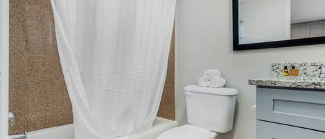 A bathroom with a bathtub, toilet, and a mirror.
