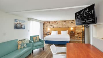 A hotel room with a bed, a teal sofa, a wooden table, and a brick-patterned wall.