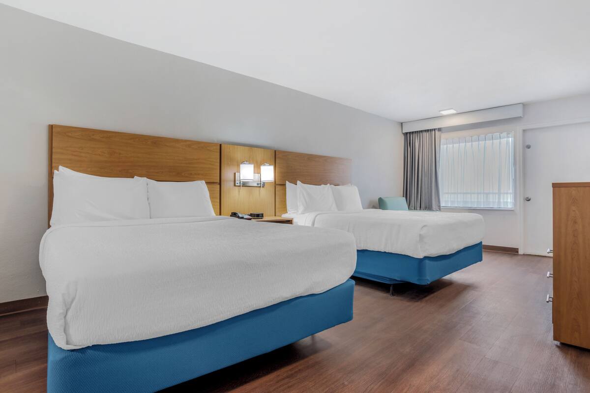 A hotel room with two beds, wooden headboard, nightstands, and a window with curtains.