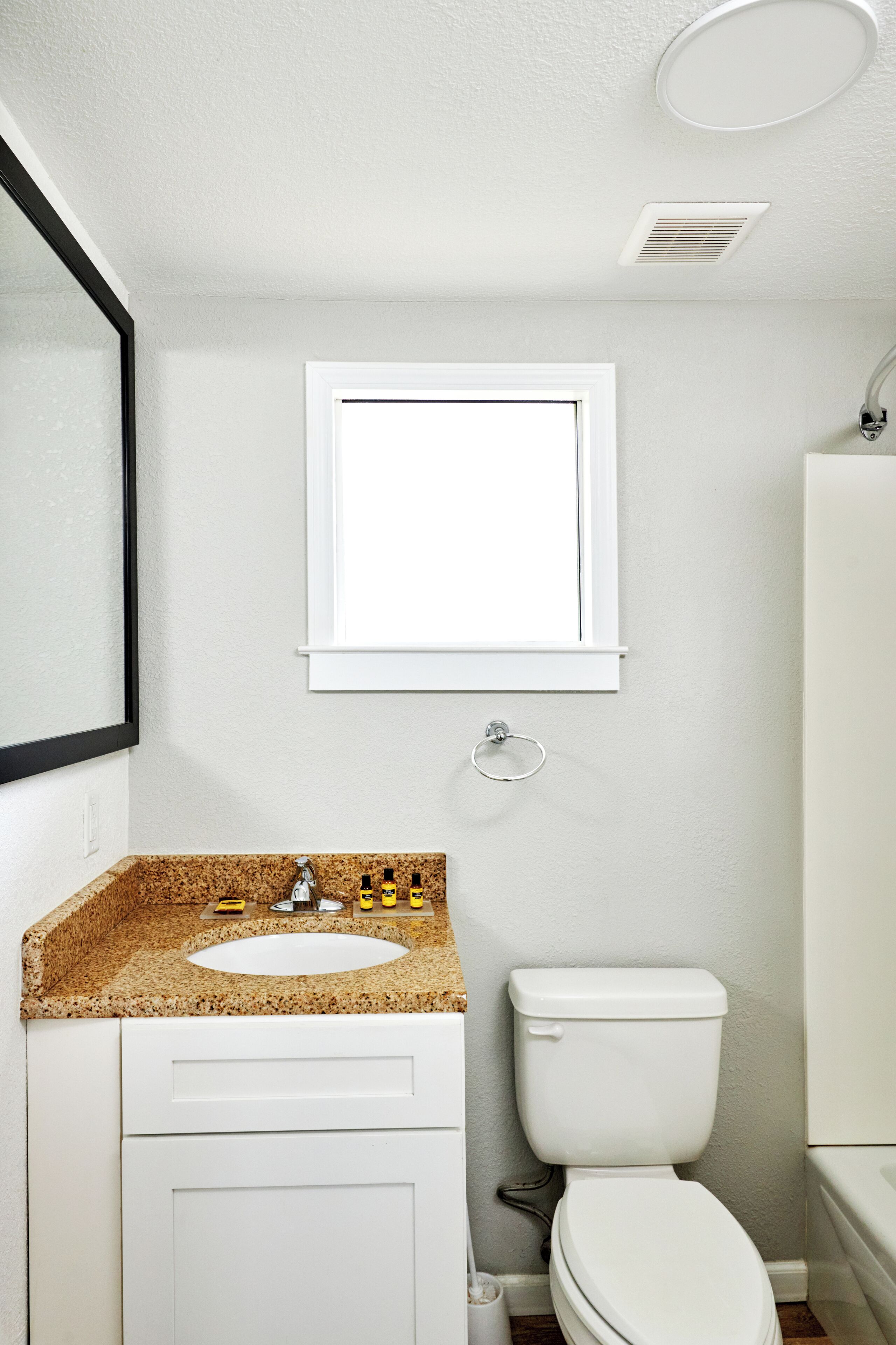 Une salle de bain avec un lavabo blanc, des toilettes et une fenêtre au-dessus du lavabo.