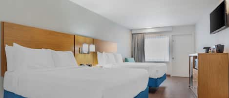 Habitación de hotel con dos camas, cabecero de madera, escritorio, televisor y ventana con cortinas.