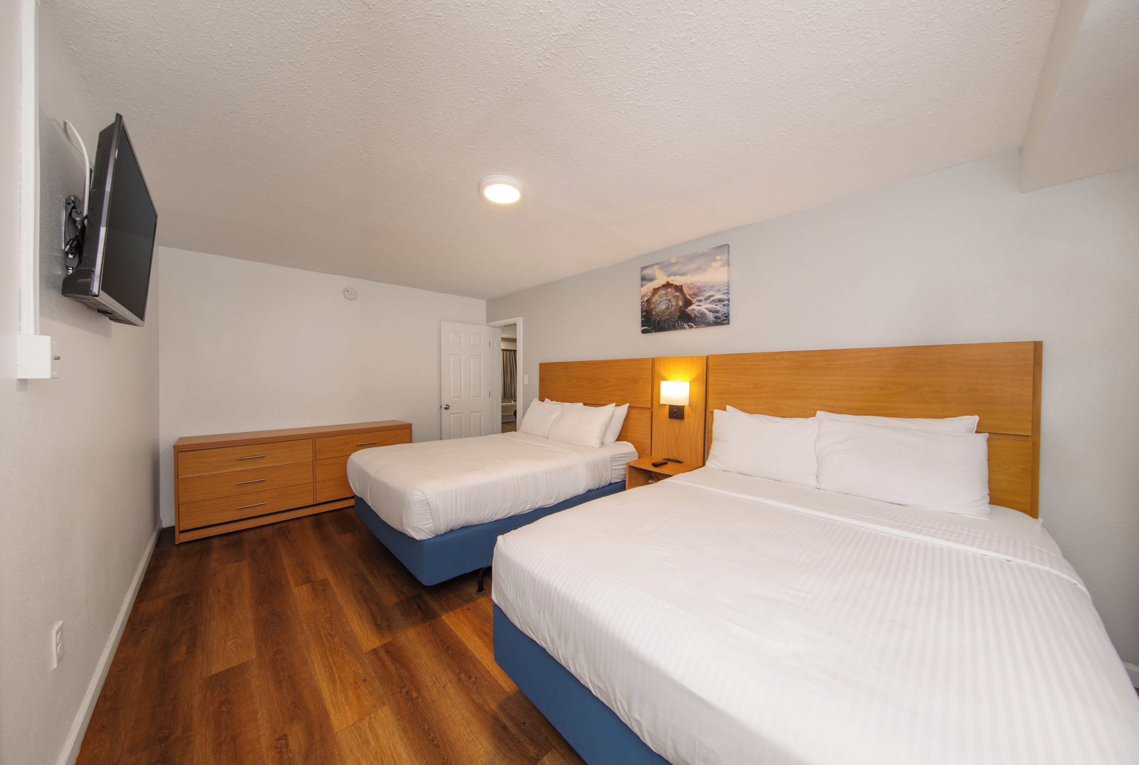 Habitación de hotel con dos camas, cabecero de madera, televisor de pantalla plana y un cuadro en la pared.
