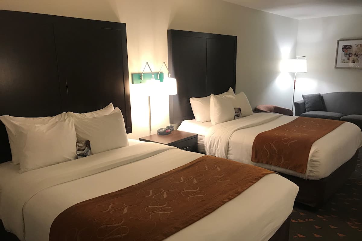 Une chambre d’hôtel avec deux lits, un bureau, une chaise, une lampe et un tableau encadré au mur.