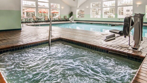 A large indoor swimming pool with a hot tub area, sunlit windows, and lounge chairs.