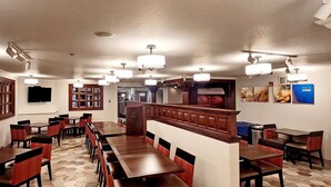 A restaurant with multiple dining tables and chairs, a wooden staircase, and a kitchen area in the background.