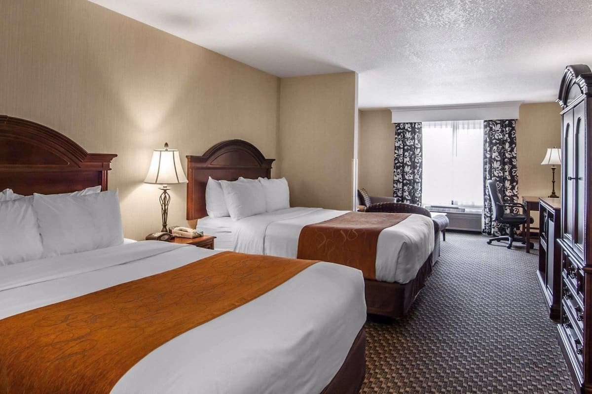 Une chambre d’hôtel avec deux lits, un bureau, une chaise et une armoire.