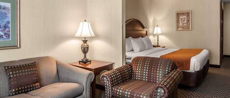 Habitación de hotel con sofá, sillón y cama con cabecera. Hay dos mesitas de noche con lámparas.