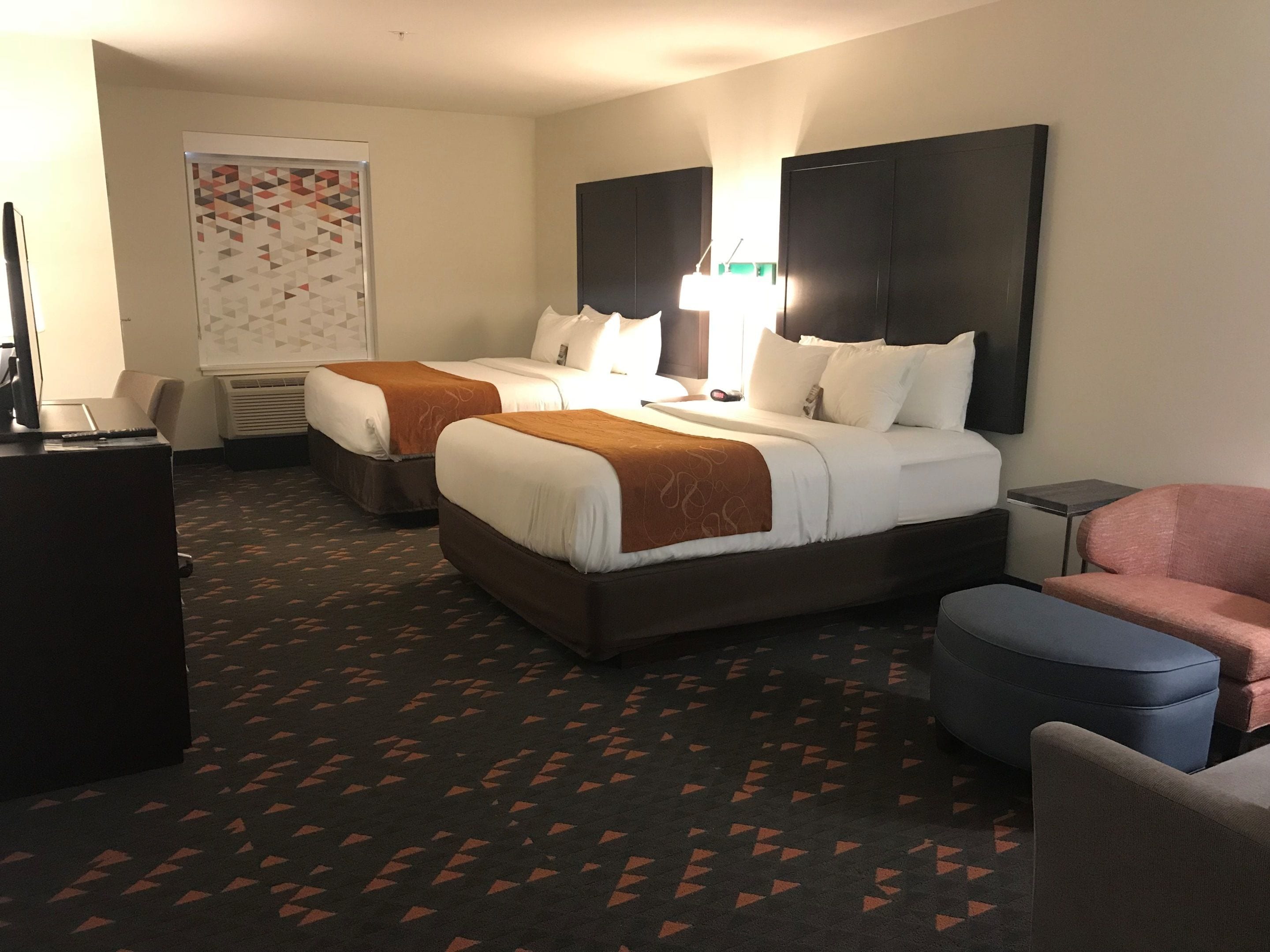 Habitación de hotel con dos camas, un escritorio, una silla y una mesita.
