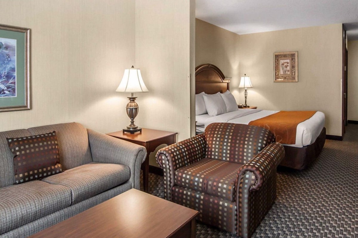 A hotel room with a sofa, armchair, bed, bedside tables, lamps, and a carpeted floor.