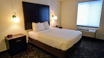 Una habitación de hotel con una cama grande, dos mesitas de noche, una lámpara de pared y una ventana con persianas.