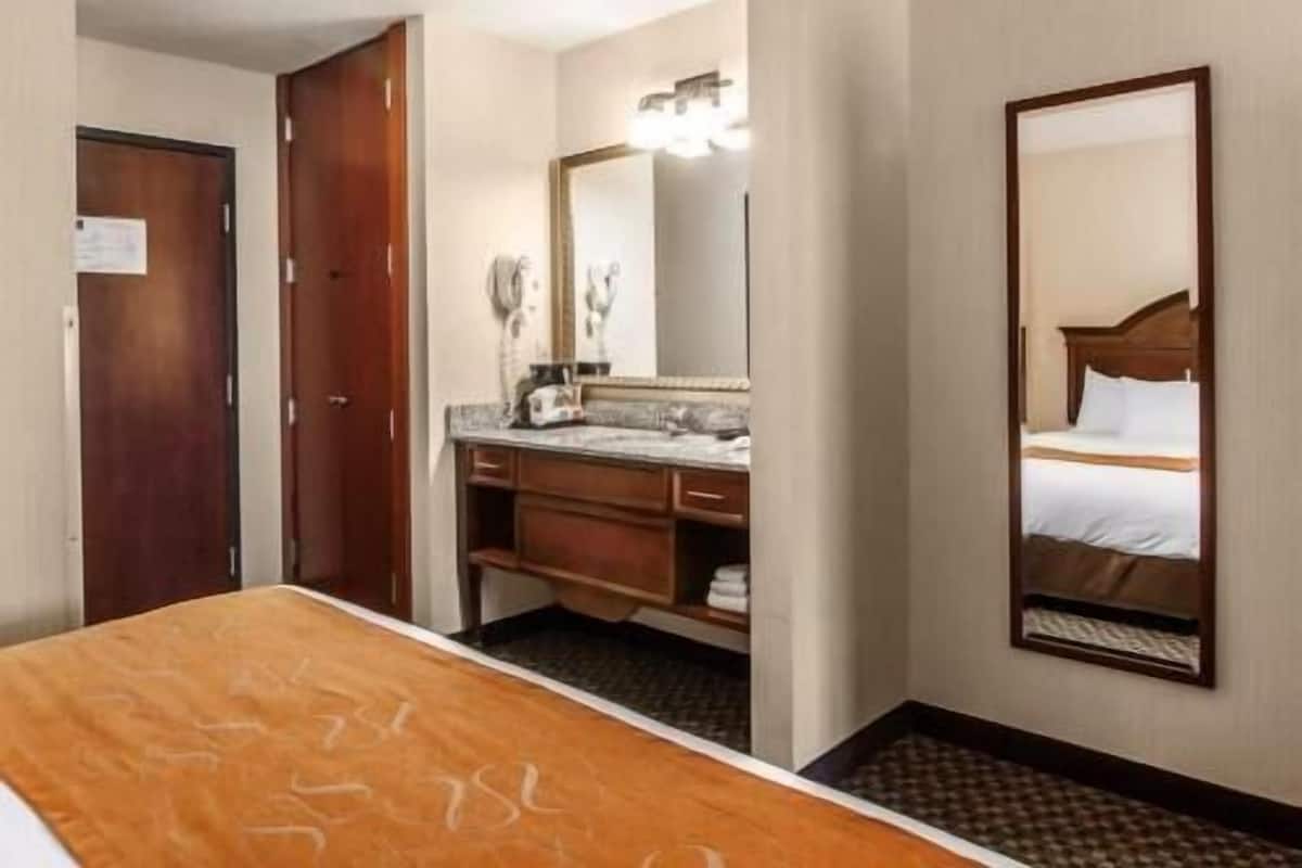 Une chambre d’hôtel avec un lit, une salle de bain avec un miroir, un lavabo et une porte.