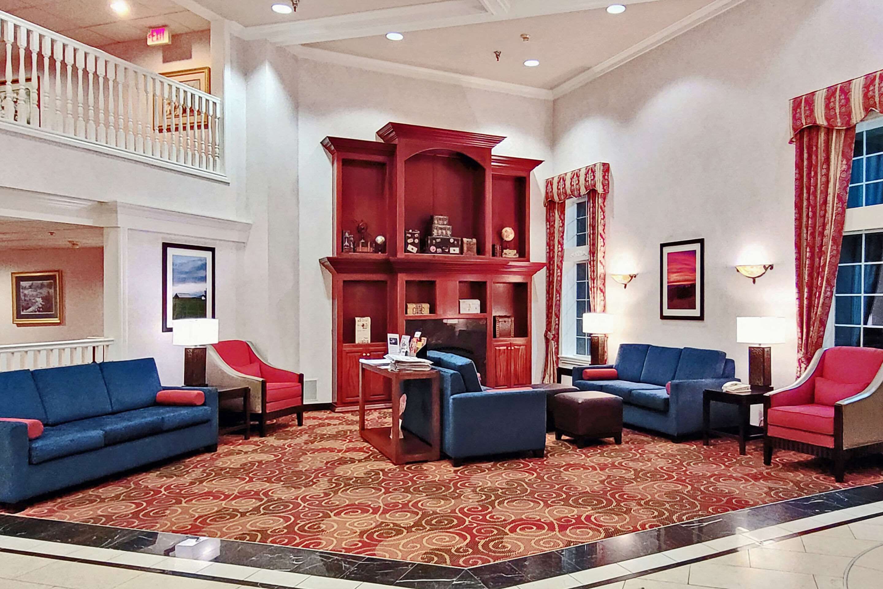 Un vestíbulo amplio con techo alto, una librería de madera roja, sofás azules y una alfombra estampada.