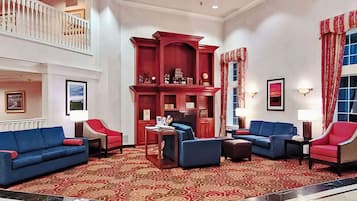 Un vestíbulo amplio con techo alto, una librería de madera roja, sofás azules y una alfombra estampada.
