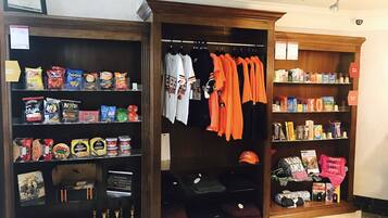 Una tienda con estantes llenos de bocadillos, un perchero con camisetas anaranjadas y una sección con distintos artículos, incluyendo un letrero de Hershey's.