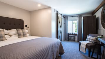 Una camera da letto con un letto grande, una scrivania e una sedia. Si vede una finestra con tende, una porta e uno spazio verde all'esterno.
