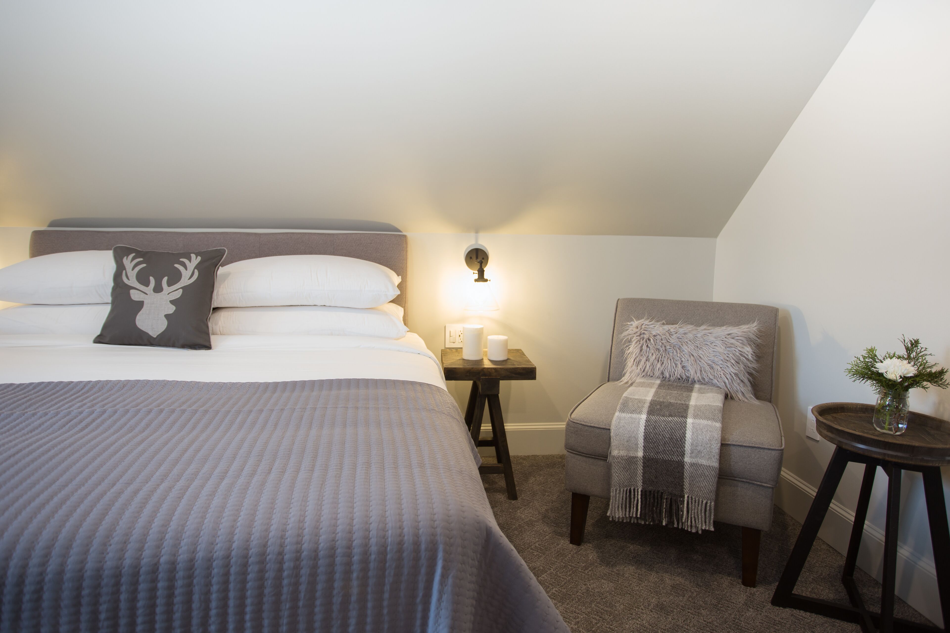 A bedroom with a bed, a nightstand, a chair, and a small table with a vase.