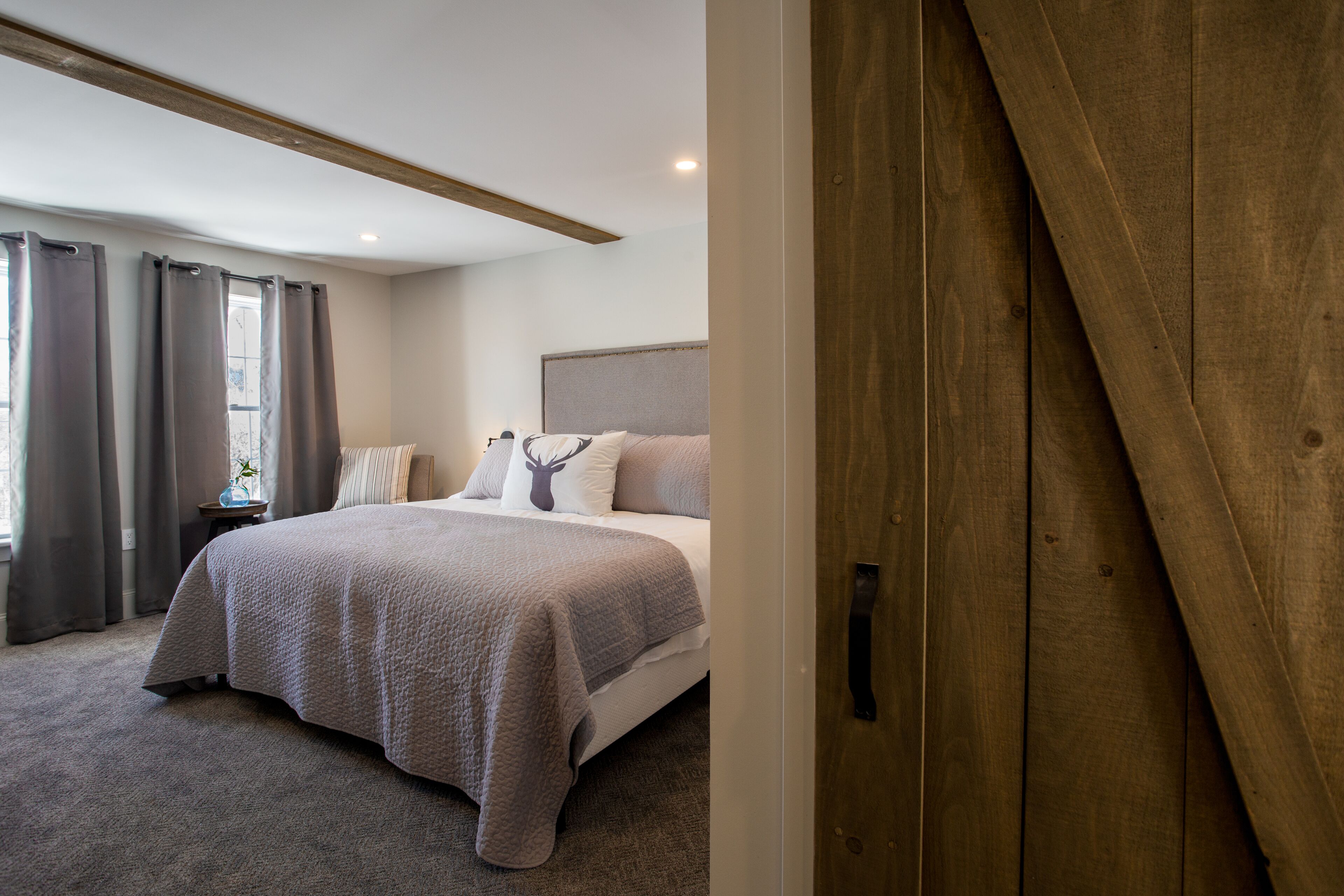 A bedroom with a bed, curtains, a nightstand, and a wooden door.