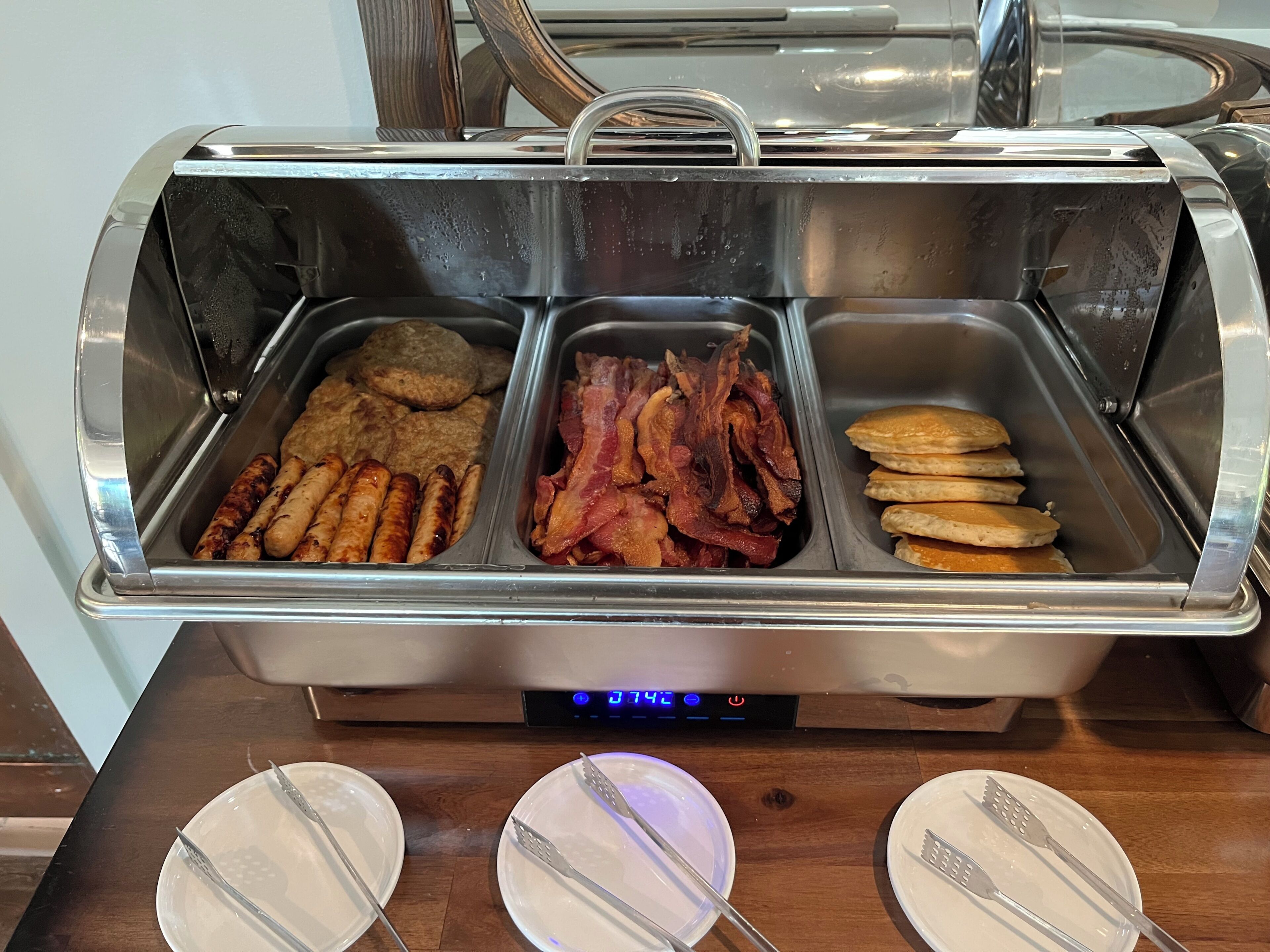 A buffet with various food options including sausages, bacon, and pancakes.