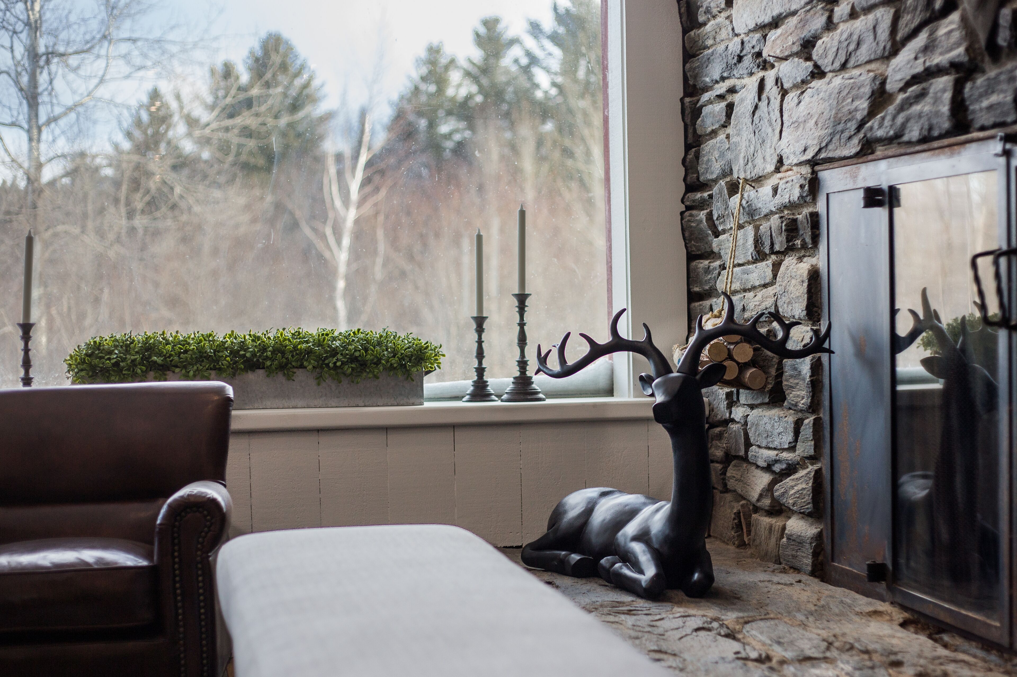 A cozy room with a stone fireplace, a leather sofa, and a deer sculpture.