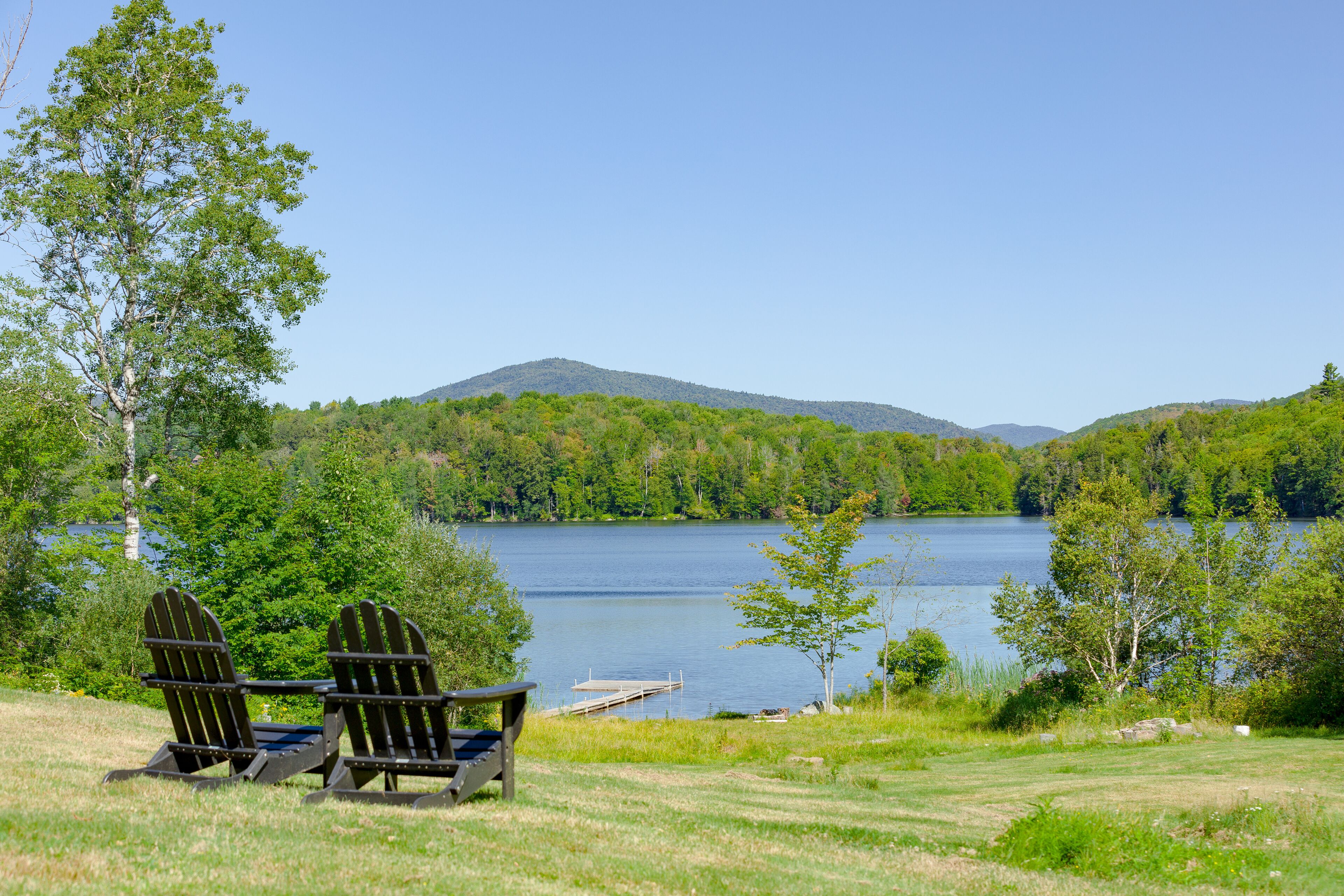 Vista al lago con dos sillas Adirondack y un muelle que se adentra en el agua.