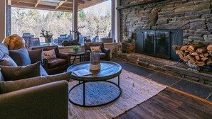 A cozy living room with a stone fireplace, leather sofas, a round coffee table, and a large window offering a view of the outdoors.