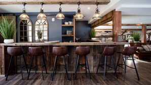 A bar area with wooden stools, pendant lighting, and a rustic ceiling.