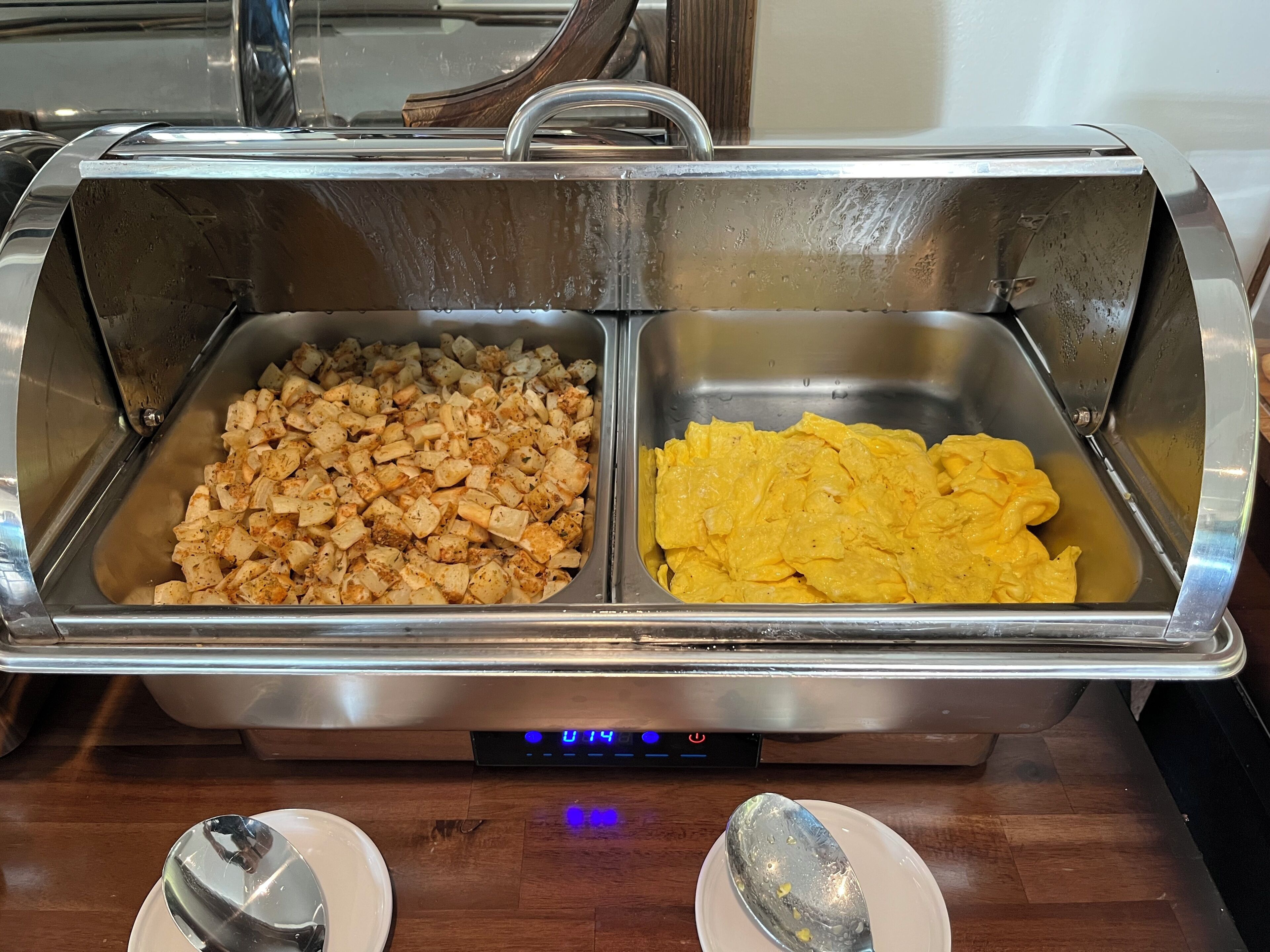 A buffet setup with two food trays, one containing cubed food and the other containing scrambled eggs.