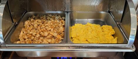 A buffet setup with two food trays, one containing cubed food and the other containing scrambled eggs.