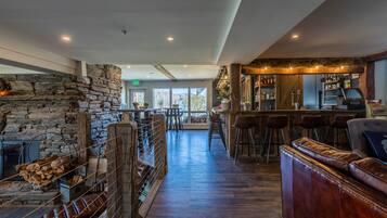Un rincón de bar acogedor con pared de piedra, mobiliario de madera y vistas al exterior.