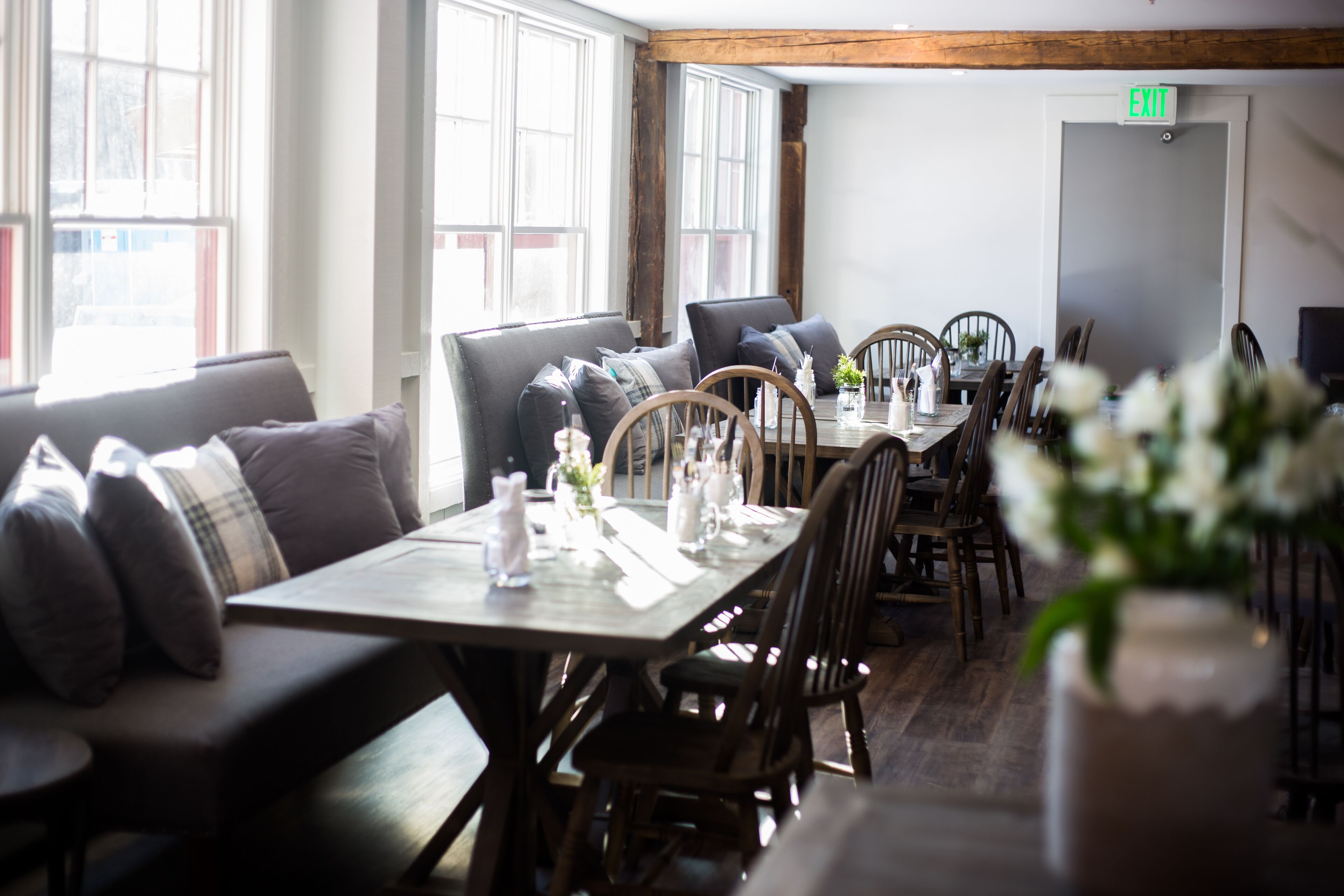 A restaurant with a long wooden table, cushioned seating, and large windows.