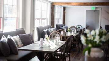 A restaurant with a long wooden table, cushioned seating, and large windows.